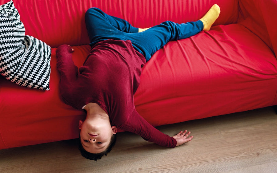 A person lies upside down on a red sofa.
