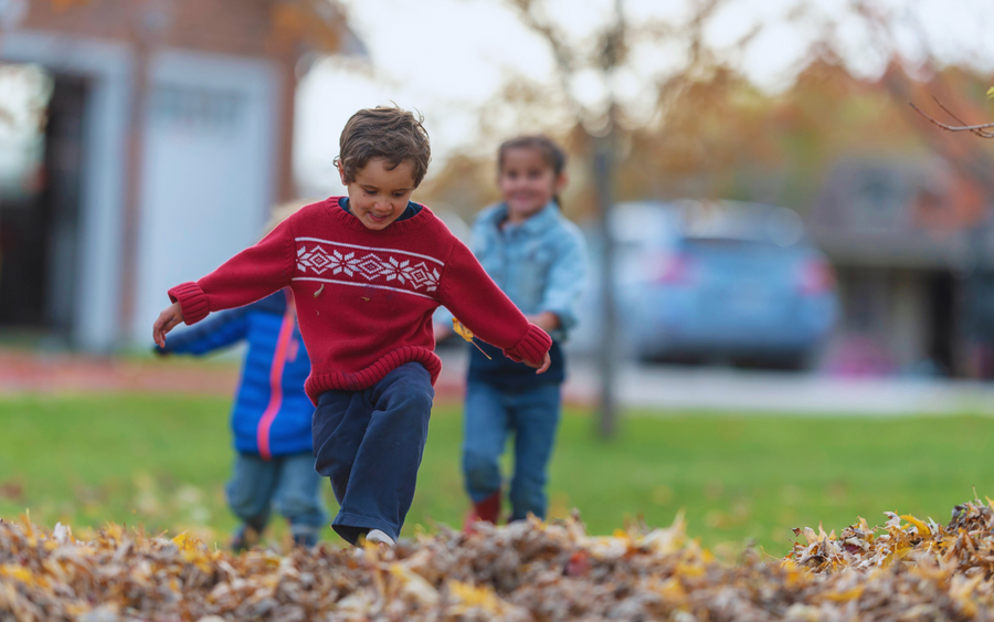Children run through fallen leaves on an autumn day.
