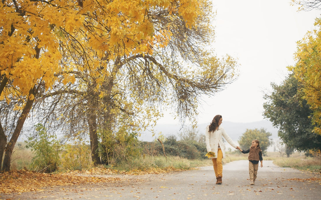 An adult and child walk together beneath yellow autumn trees.