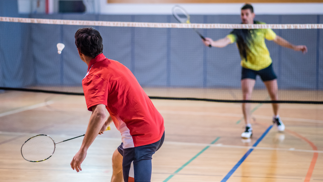 Two people play badminton across an indoor court.