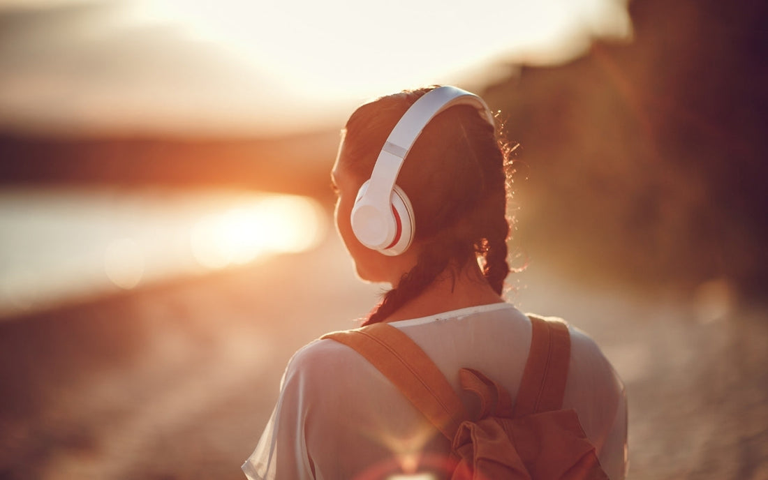 A person in headphones looks across water at sunset.
